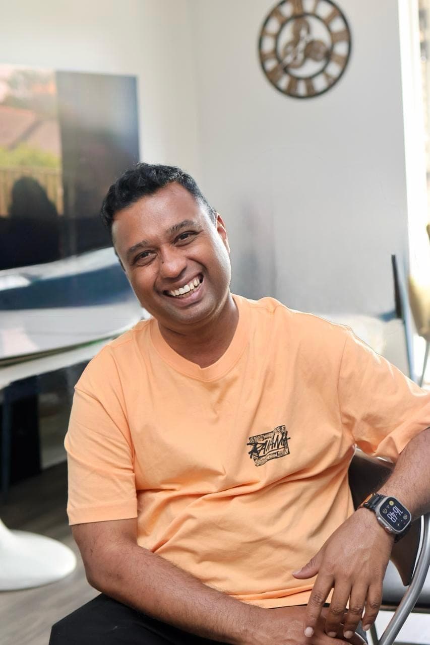 Srini smiling at home in a relaxed orange T-shirt